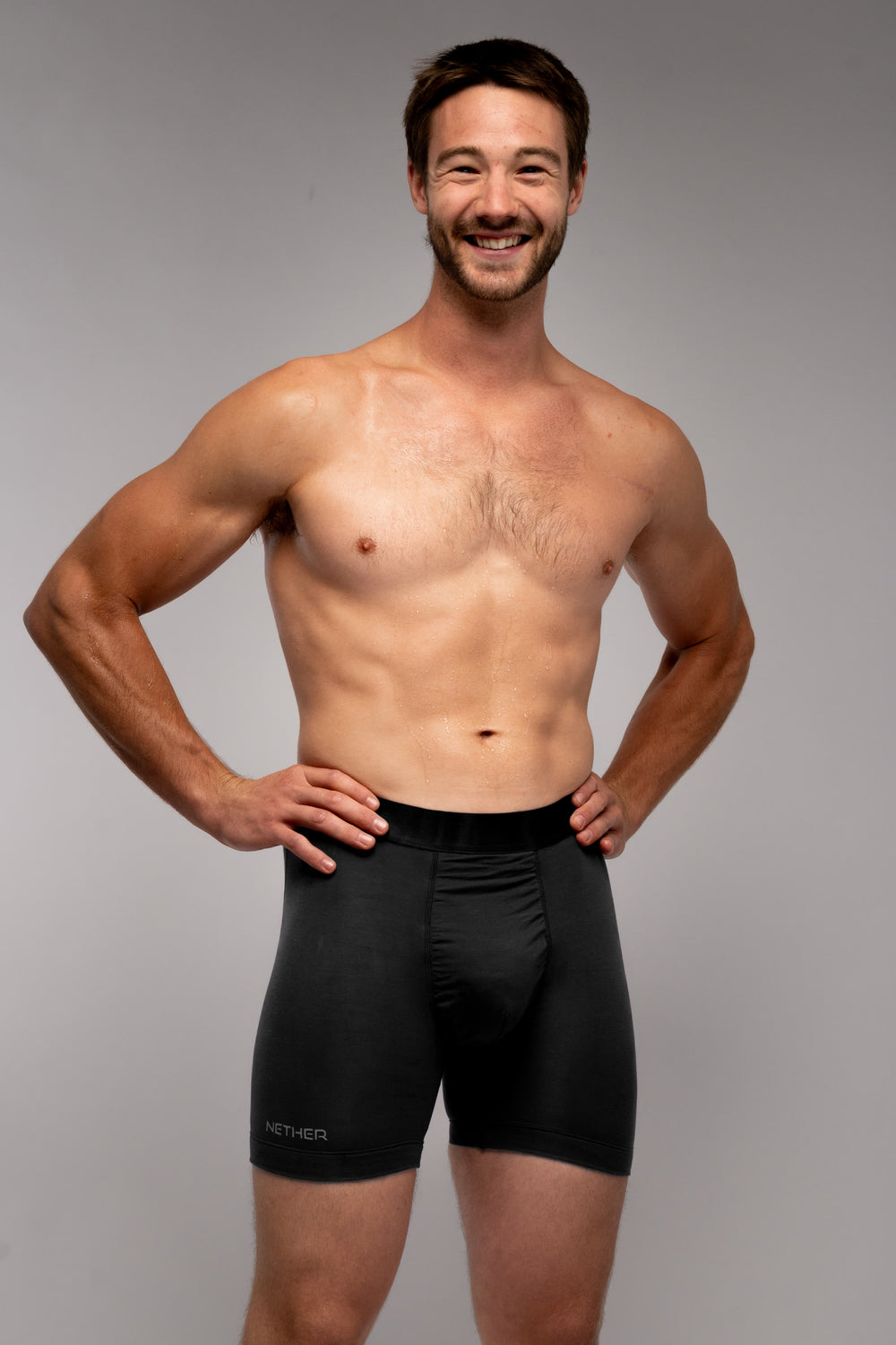 A man standing with his hands on his hips wearing the Nether Roam Boxer Brief in Midnight, on a grey studio background