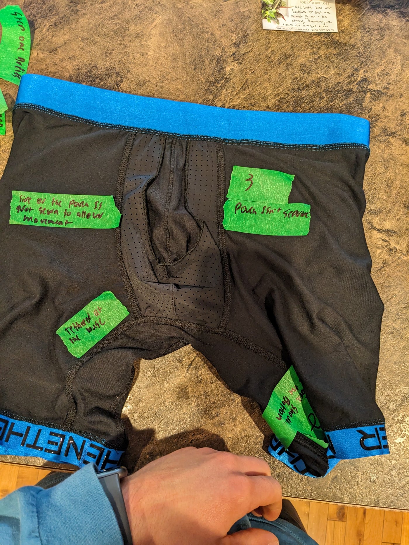 A black sample boxer brief with a blue waistband, covered in green masking tape carrying hand-written notes to the factory