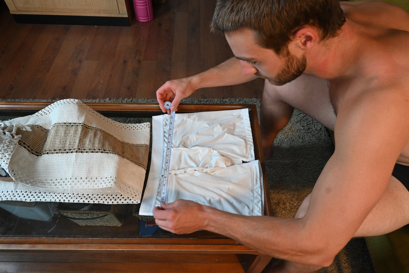 Stephen leaning over a coffee table measuring a pinned white prototype with a tape measure