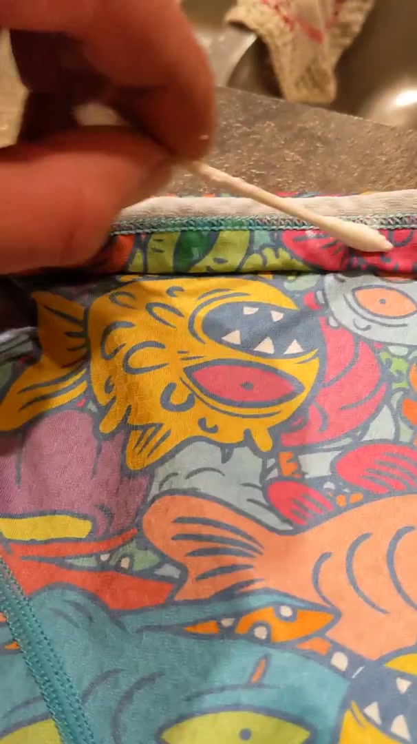 A cotton swab held over the printed waistband of a pair of boxer briefs, mid-way through gluing grip strips on by hand